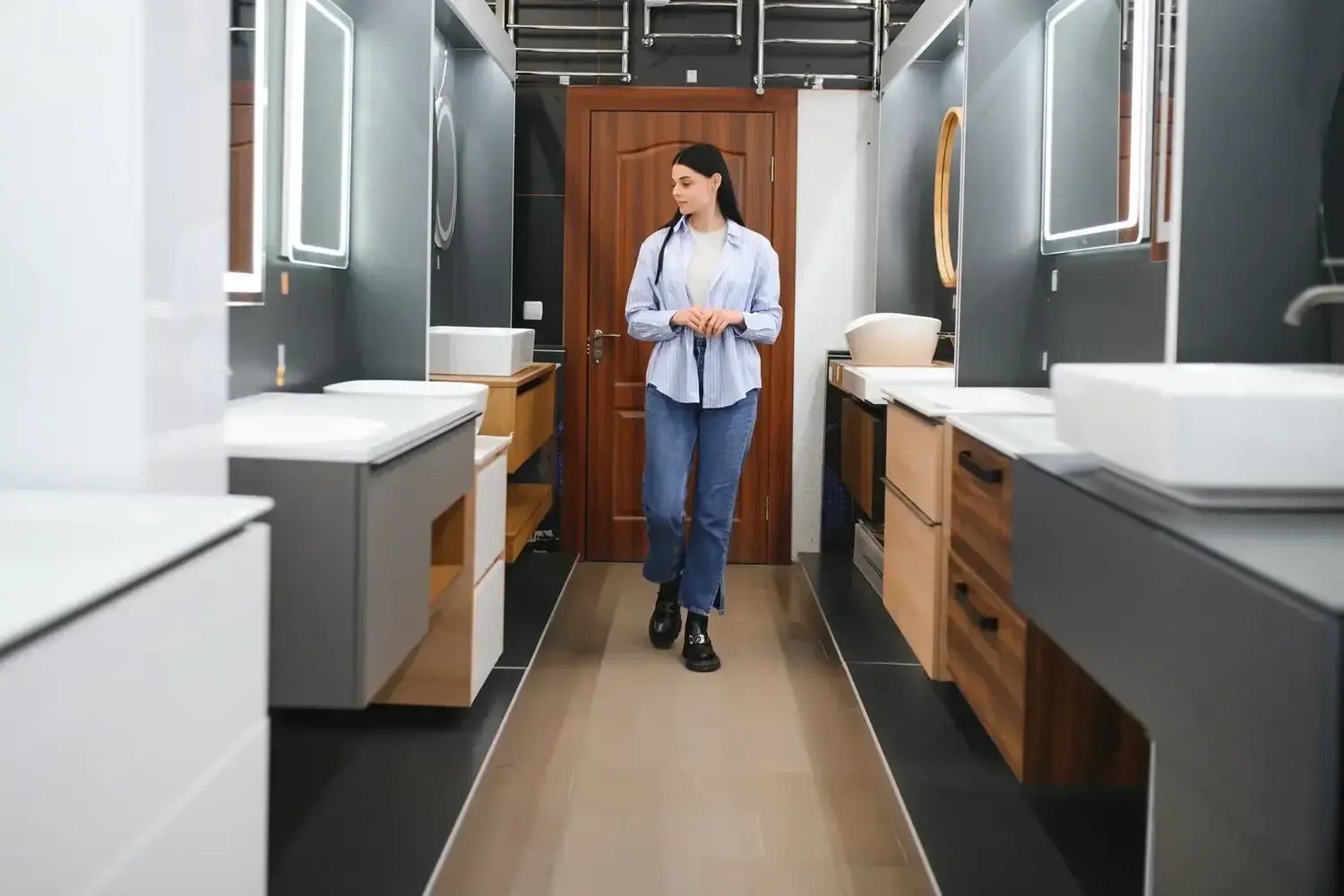 A woman with long dark hair walks down a showroom aisle featuring modern bathroom fixtures.